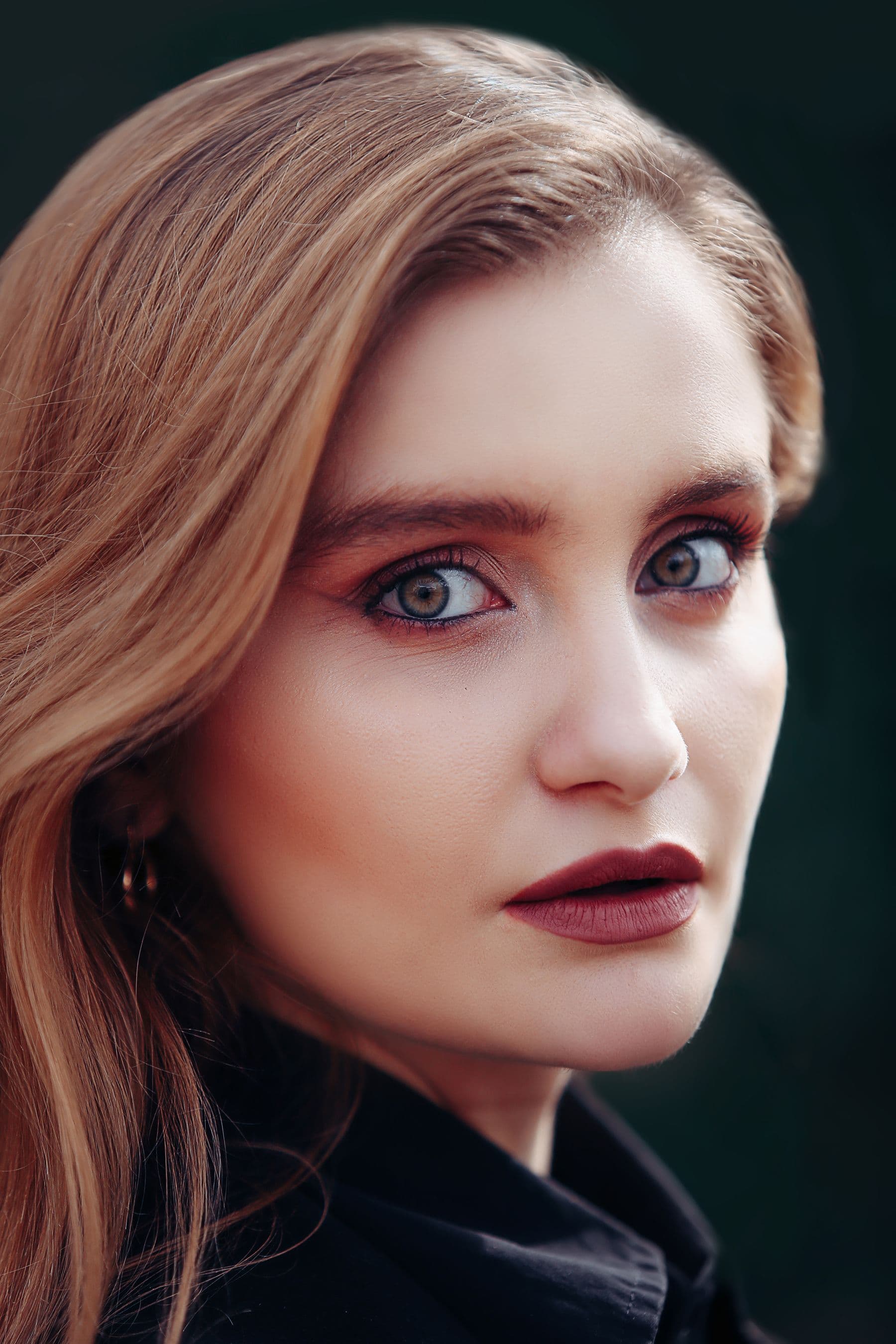 Editorial beauty portrait with deep mulberry lip color against a dark backdrop