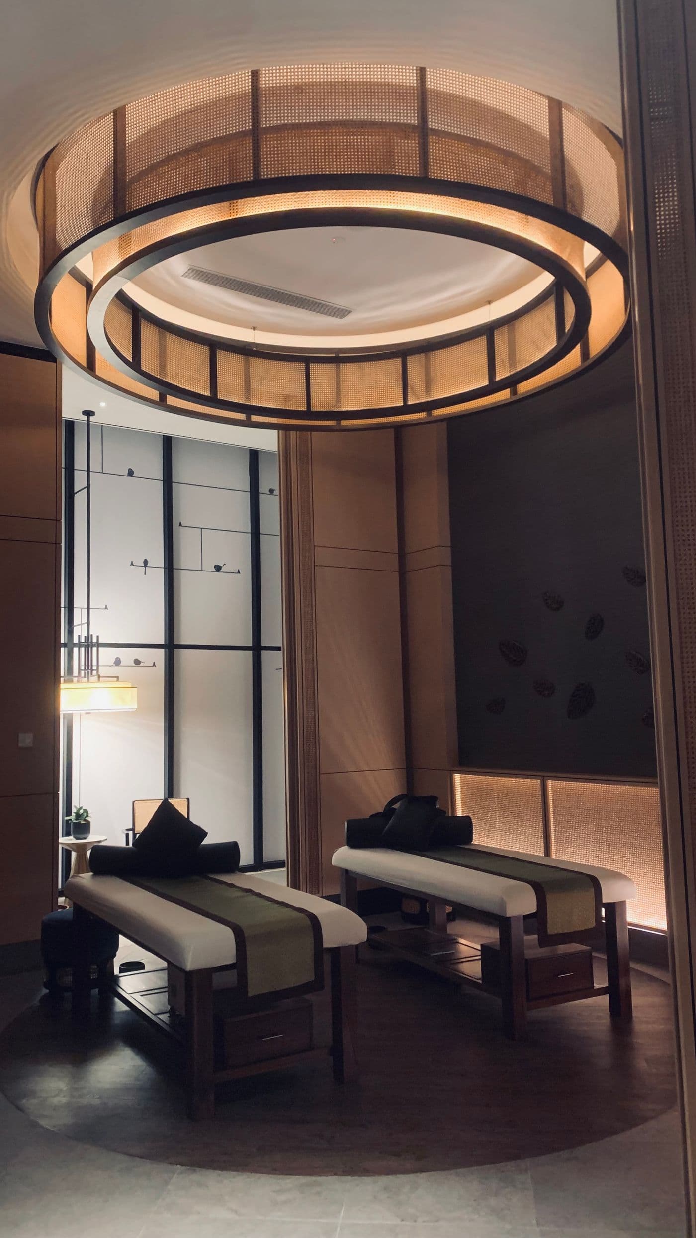 Dim treatment suite with a circular rattan chandelier over two treatment beds