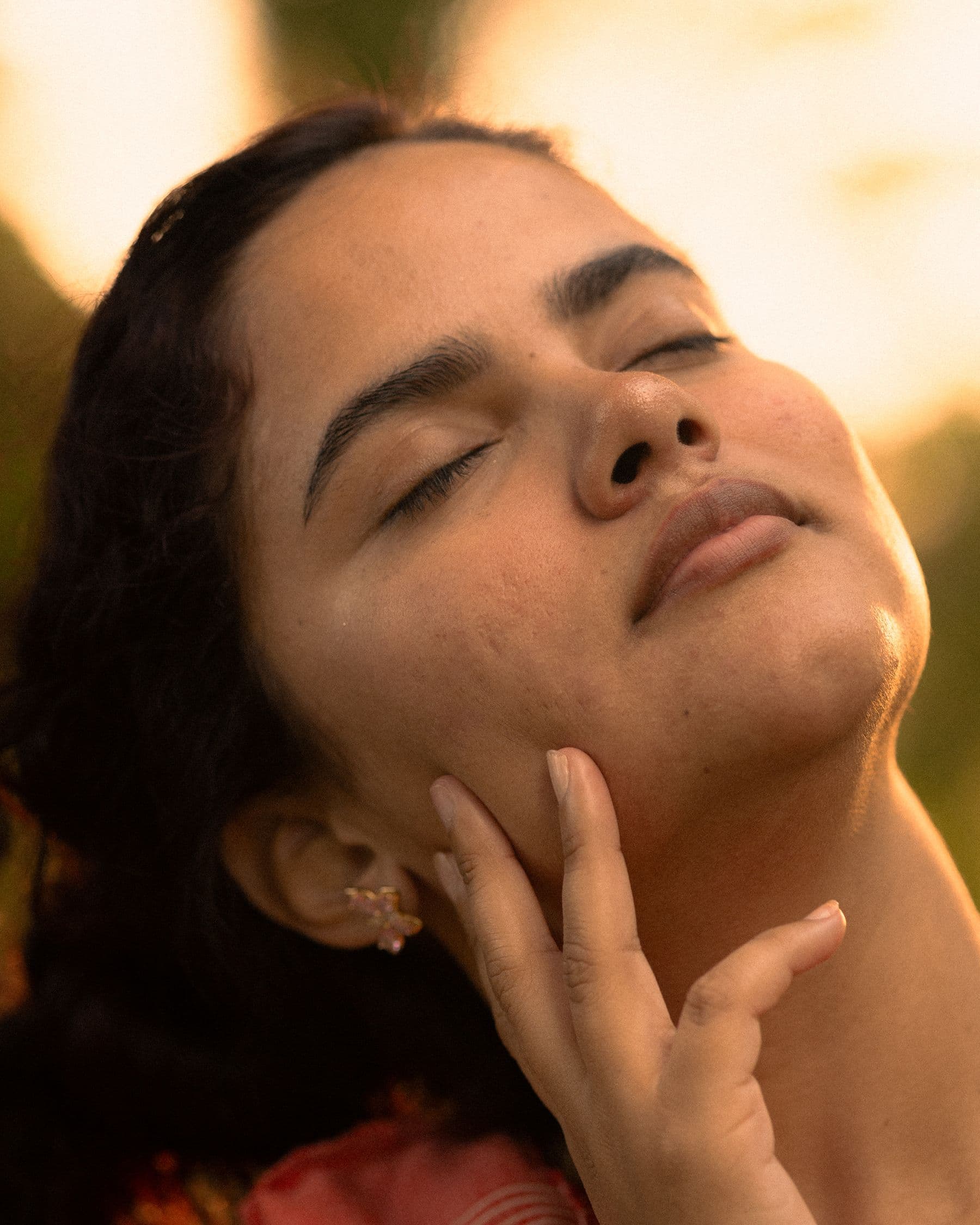 Golden hour skincare portrait, eyes closed, fingertips resting along the jawline
